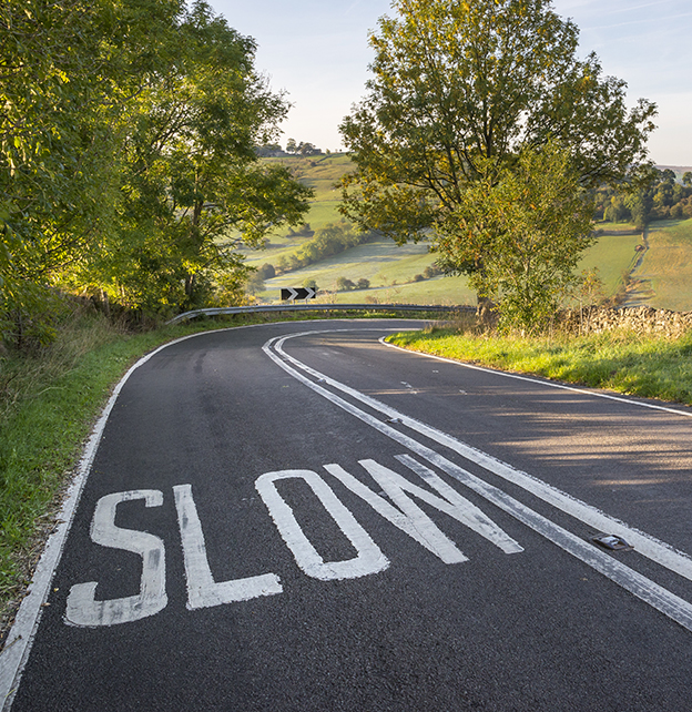 The word "slow" written on a paved road in the countryside