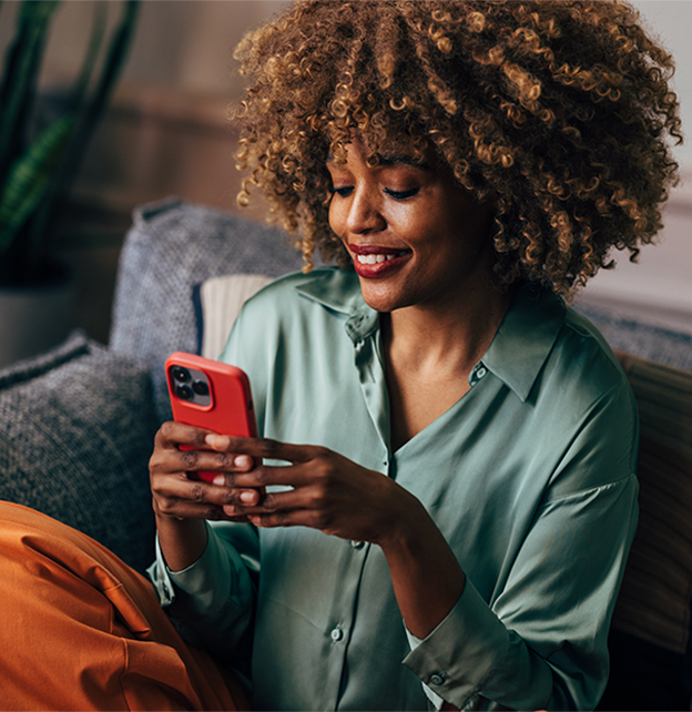 Woman sat on sofa looking happily at her phone