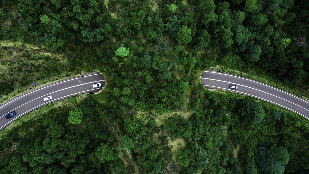 Aerial view of cars entering and exiting a tunnel passing through a verdant green hillside